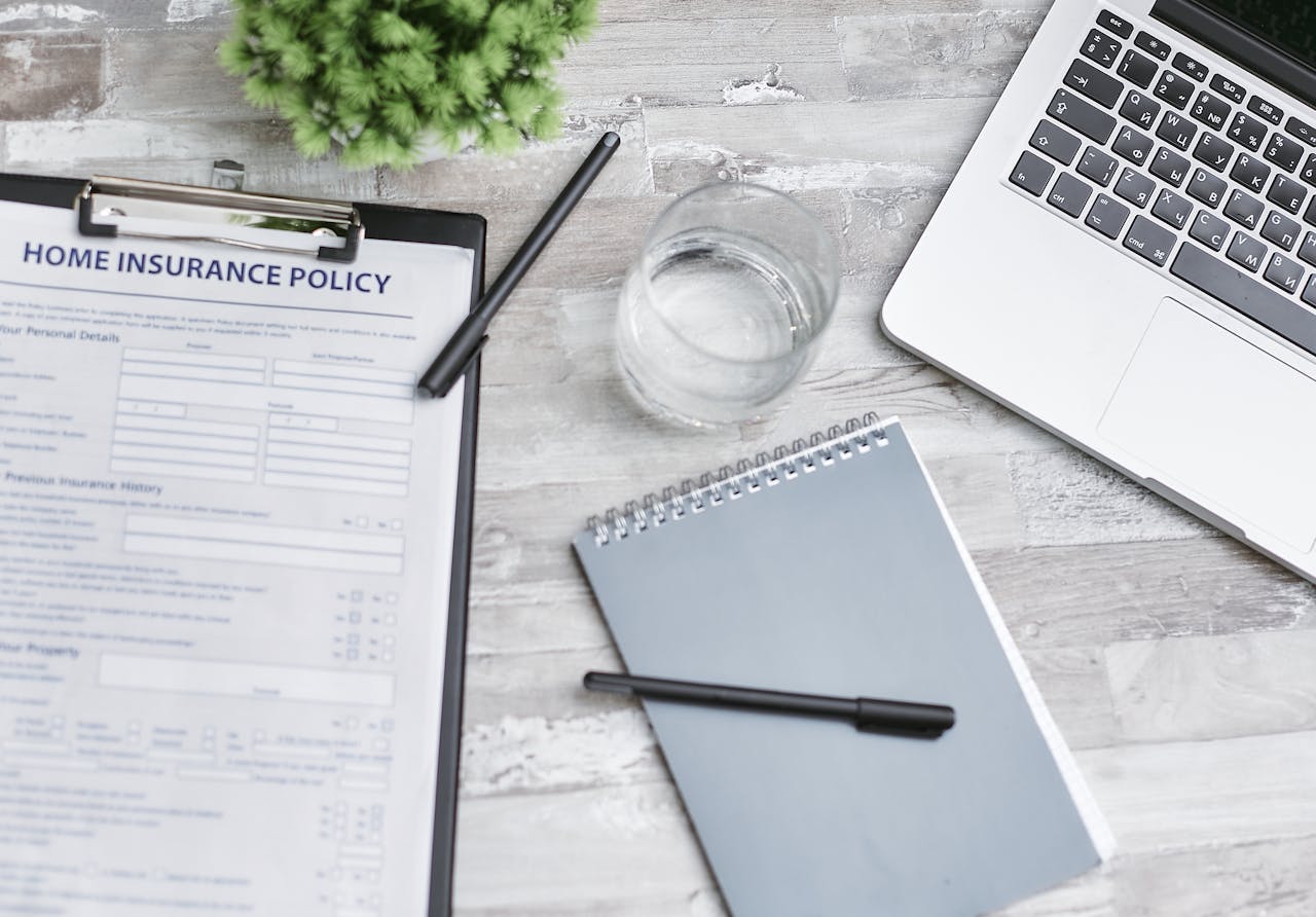 Flat lay of a workspace with a home insurance policy, laptop, and notebook on a desk.